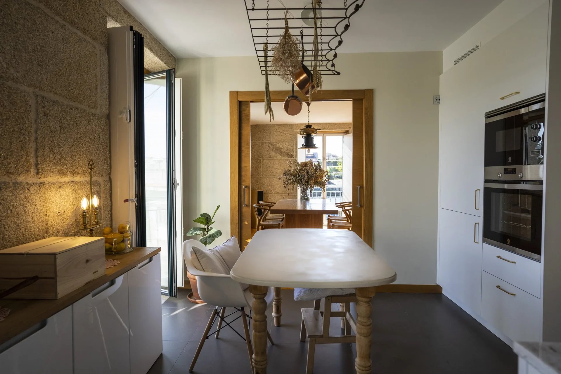 Comedor reformado en Corbaceiras, Pontevedra. Muros de piedra vista, suelo de madera natural, butaca redonda blanca y escultura de bronce. Interiorismo de Eva Penado the Studio.