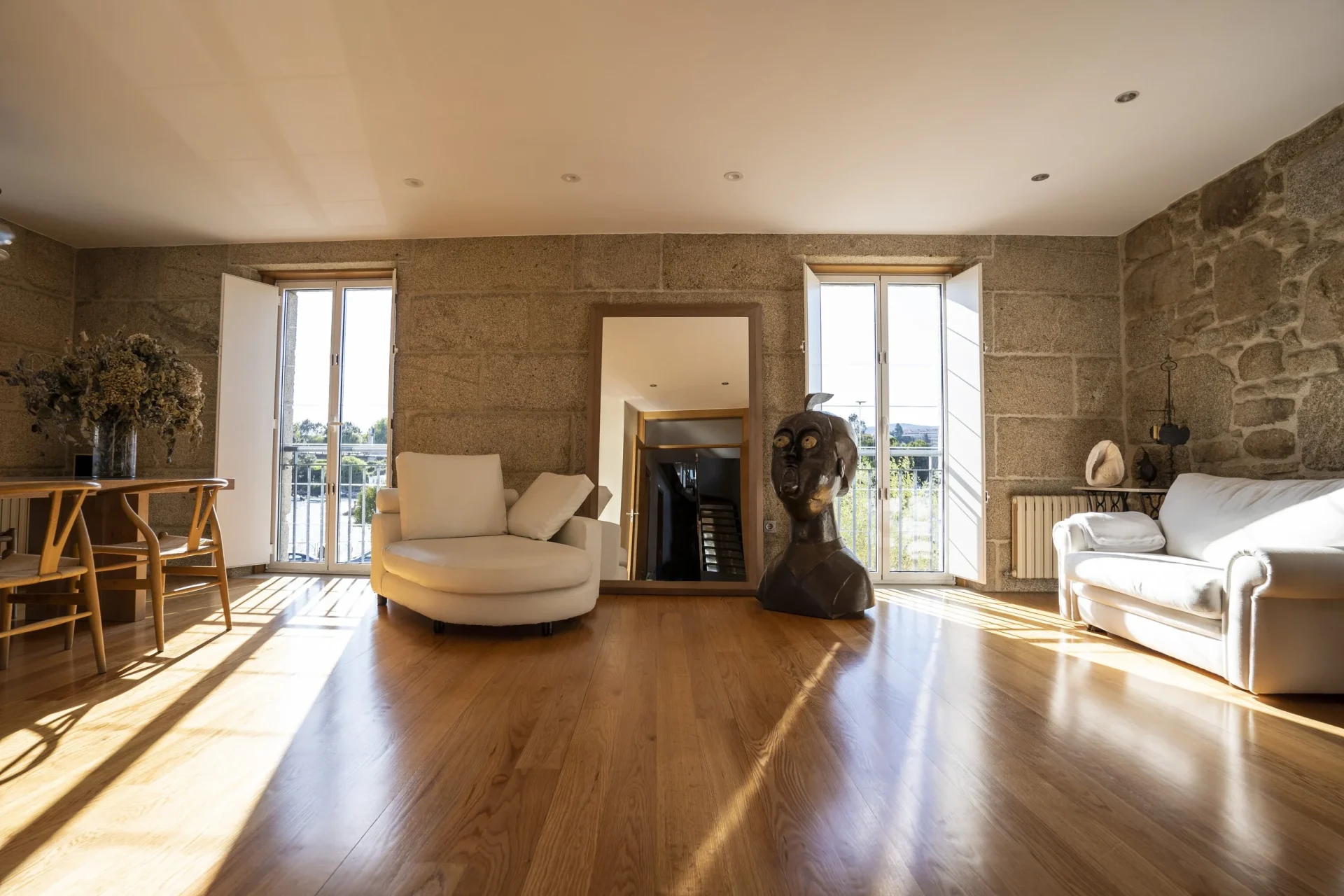 Salón de piso reformado en Corbaceiras, Pontevedra. Muros de piedra vista, suelo de madera natural, butaca redonda blanca y escultura de bronce. Interiorismo de Eva Penado the Studio.